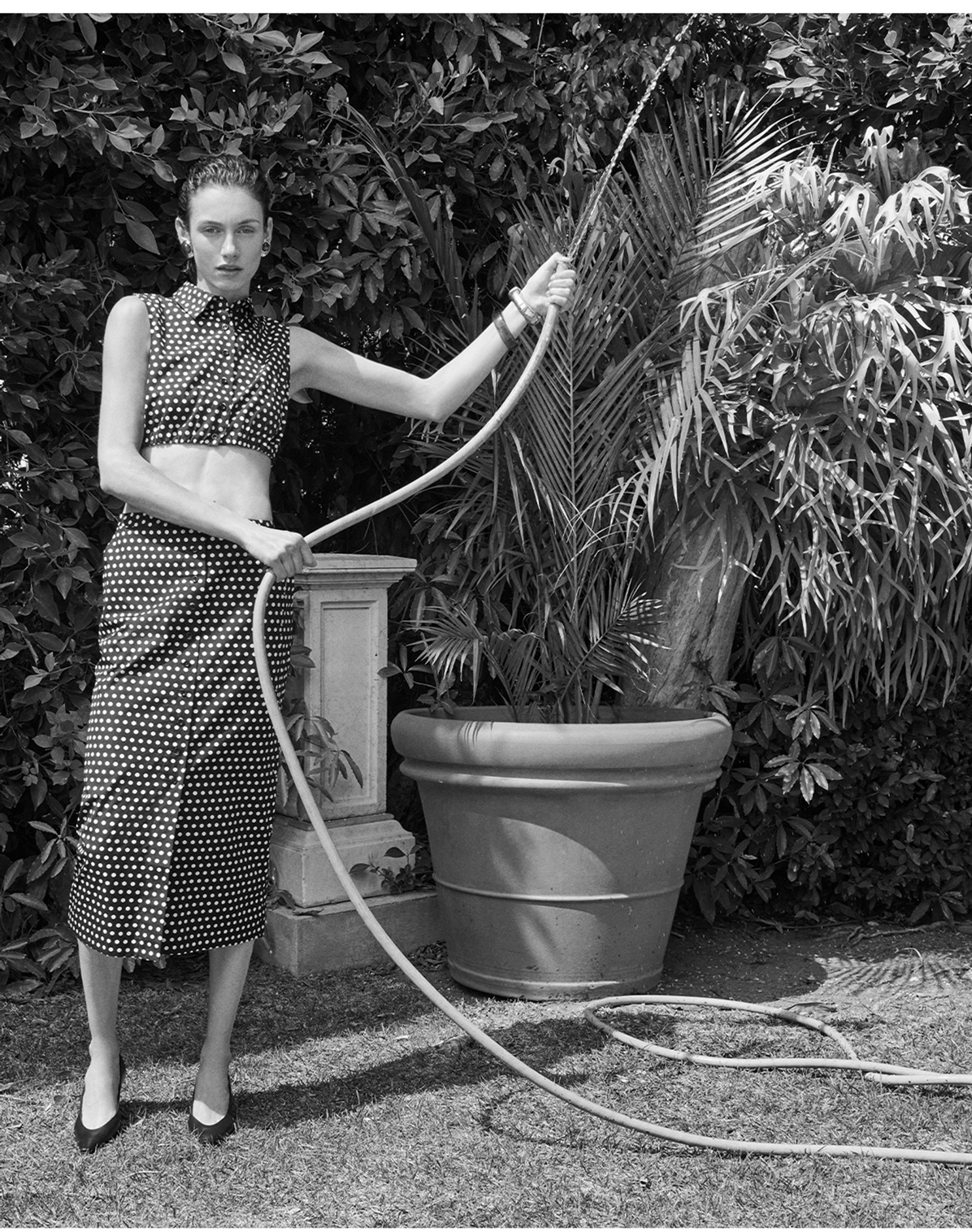 A model in black and white polka dots in a garden with a watering hose