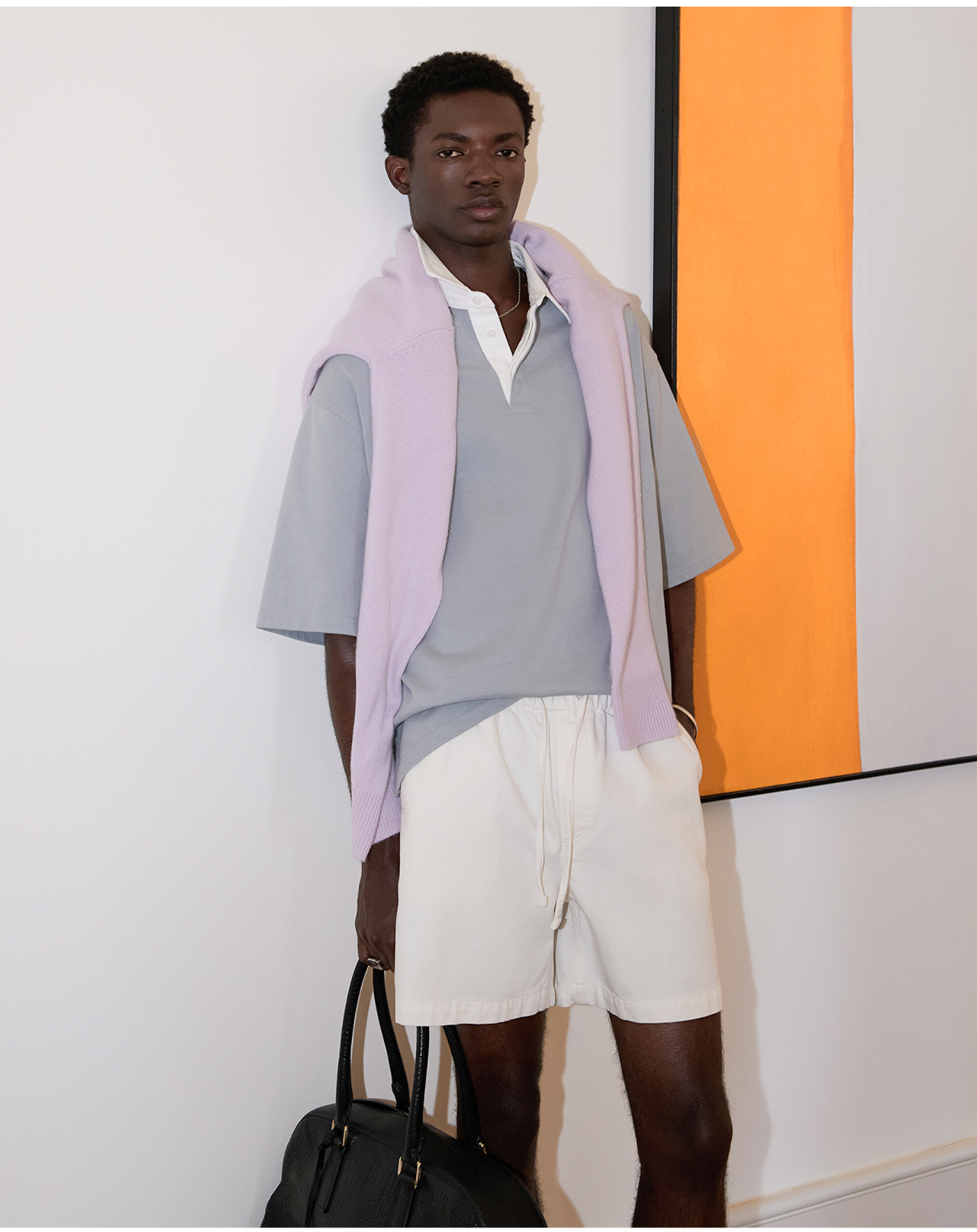 Model in white drawstring pants with a blue polo and lilac sweater over his shoulders