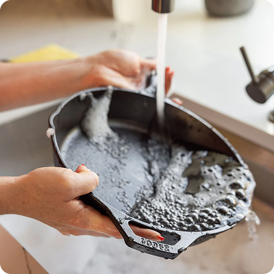 A cast iron skillet being washed with soap and water