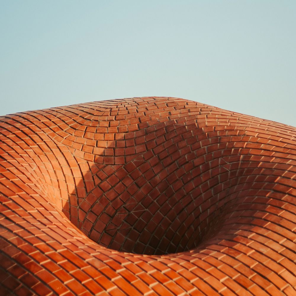 A curved surface of red bricks with a deep hole descending out of sight in the center. 