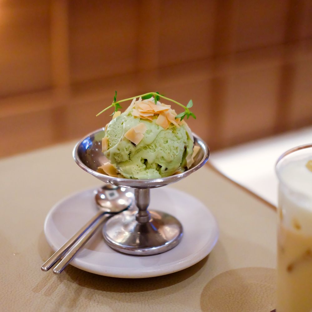 A scoop of green ice cream topped with sliced garlic, served in a silver goblet.