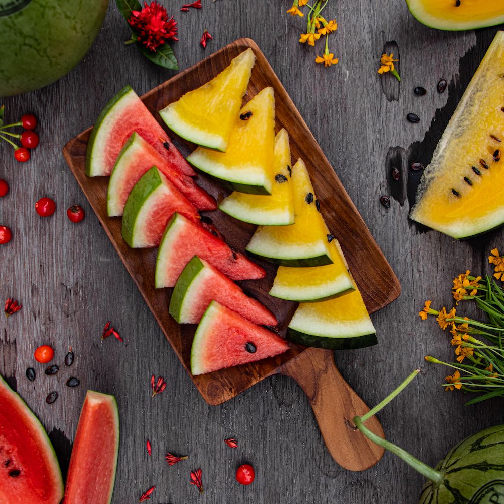 Slices of red and yellow watermelon lined up neatly on a wooden cutting board.